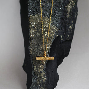 Delicate gold necklace on black and gold mineral rock, 18ct gold t-bar pendant decorated with intricate texture resembling mineral stritations