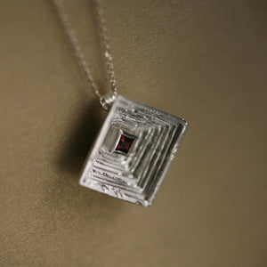Corona Laminae textured 18kt white gold statement pendant necklace with dark pink rhodolite garnet princess, angled view.